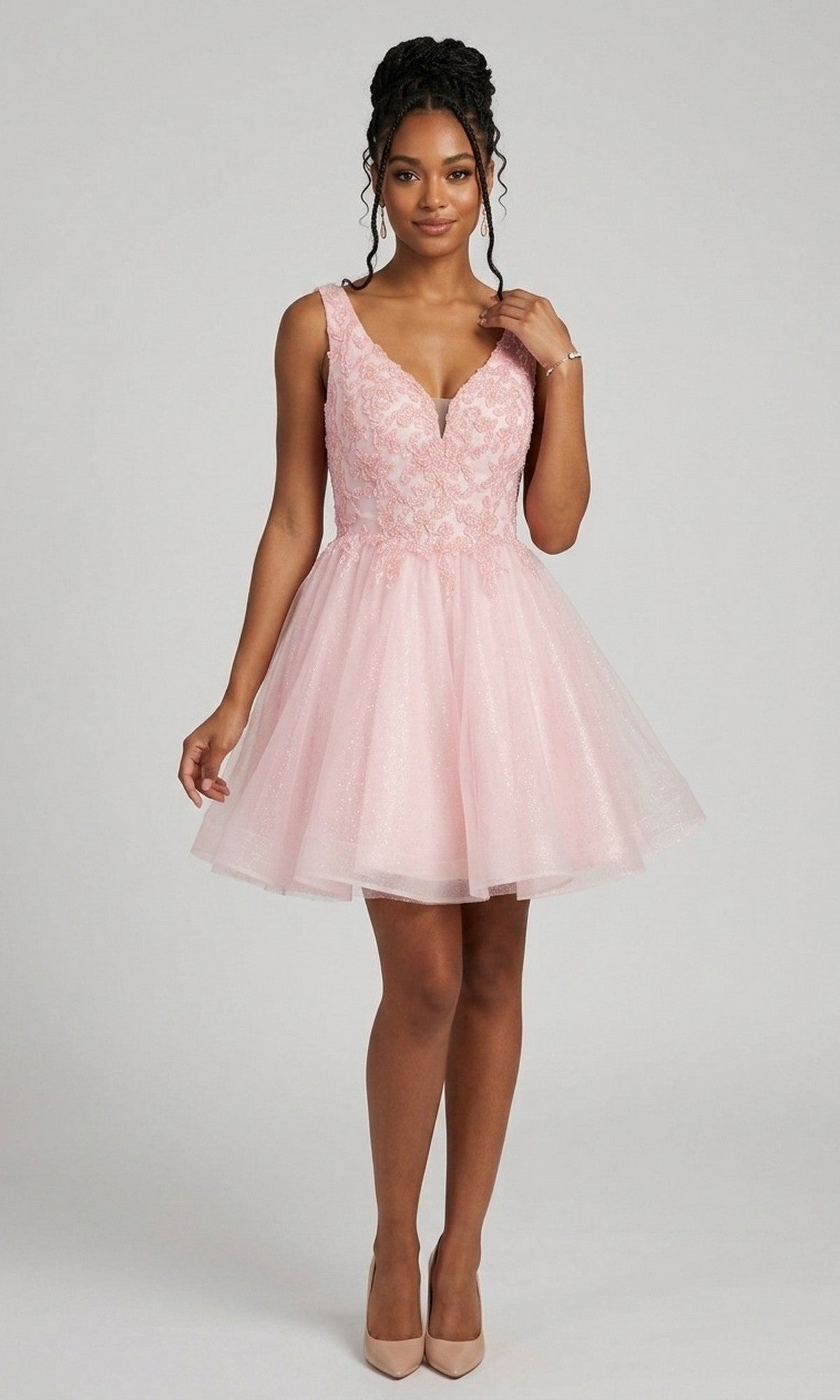 A woman wearing the Chicas C376 Short Homecoming Dress in pink—a sleeveless, knee-length fit-and-flare style featuring a lace bodice—paired with nude heels, stands against a plain light gray background.